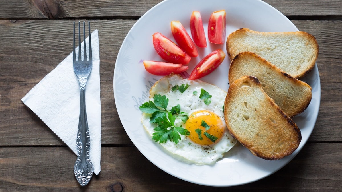 fried eggs with toast and tomatoes on wooden table around fork