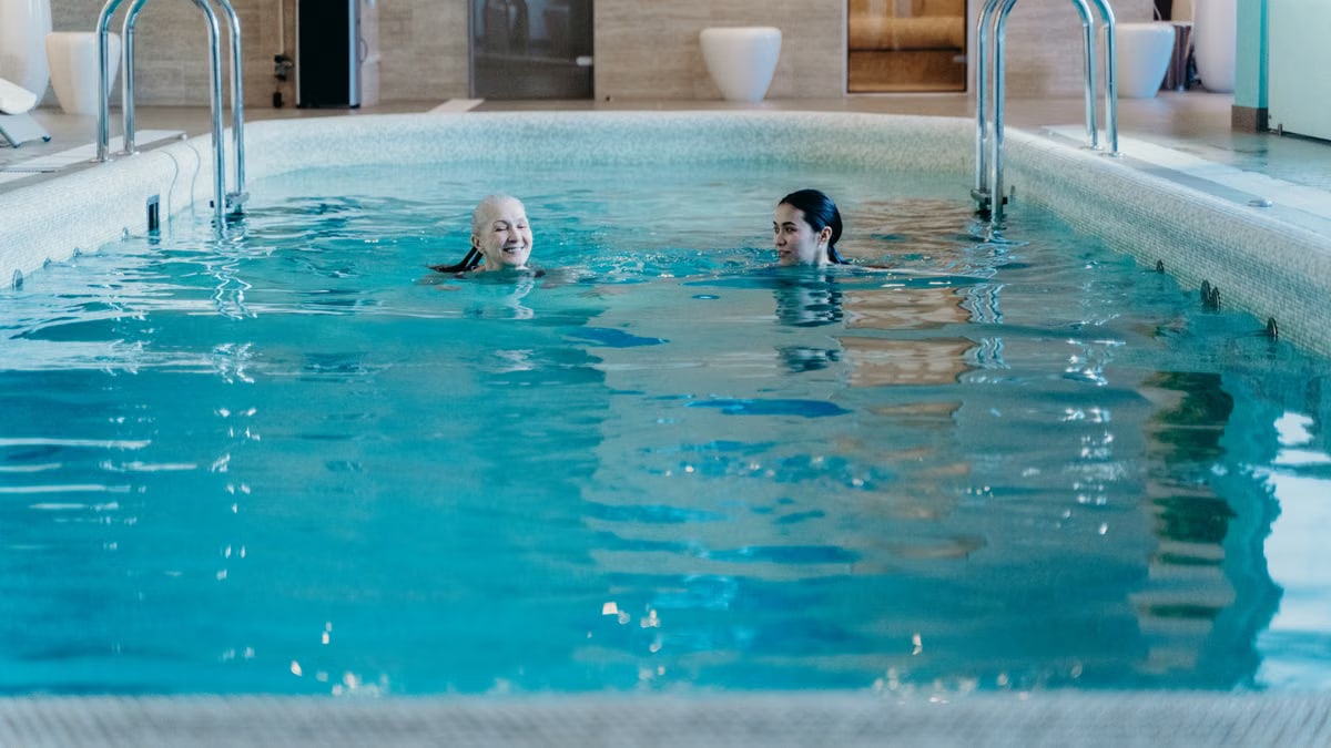 Senior woman and adult woman enjoying a relaxing swim in an indoor pool, featuring leisure and relaxation.